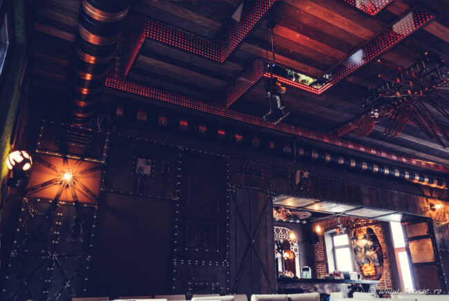 Salle voûtée de l'Enigma Café à Cluj-Napoca avec éclairage tamisé, engrenages apparents et esthétique steampunk industrielle