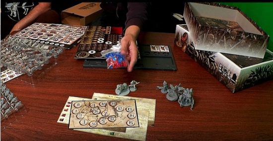 Unboxing du jeu de plateau Conan de Monolith avec dés et figurines au-dessus de la boîte ouverte