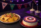 Un plateau de nachos avec des sauces colorées représentant les pierres de l'Infini, éclairées par une lumière violette. A coté Un cheesecake décoré en forme du bouclier de Captain America, entouré de petits drapeaux Avengers.
